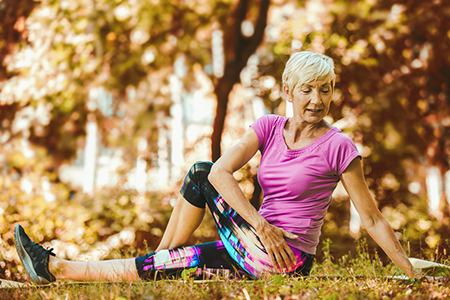 Older woman sitting on ground stretching her back.